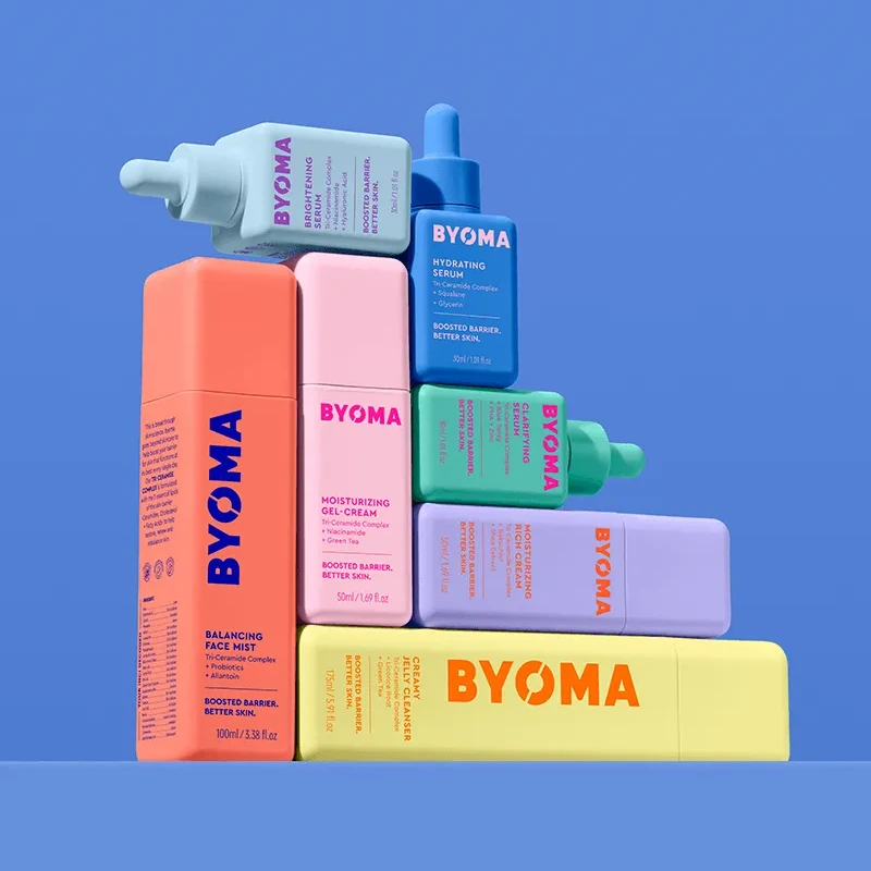 Colorful BYOMA skincare bottles stacked against the blue background of Pearlfisher’s campaign photograph