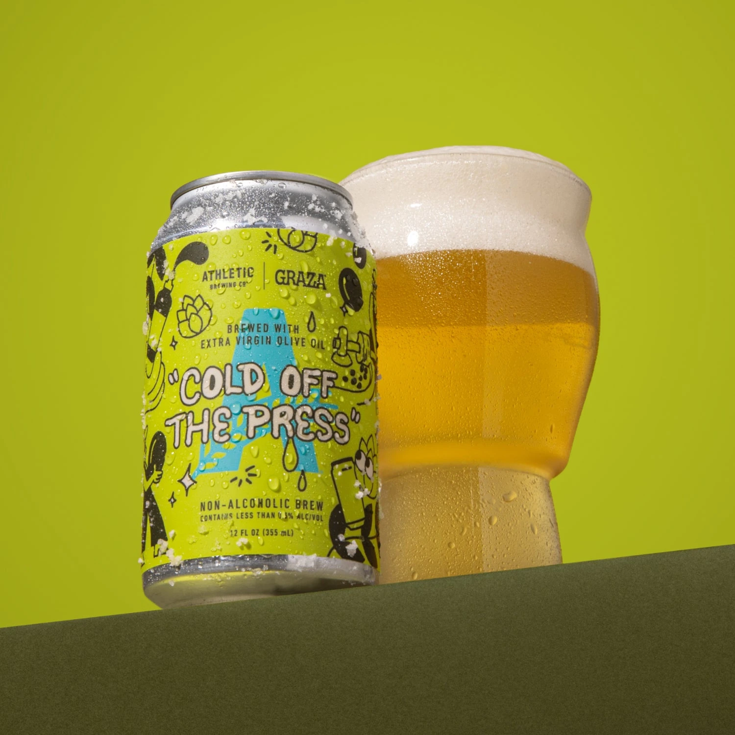 Athletic Brewing × Graza Cold Off The Press can and a glass of golden pils on a green background