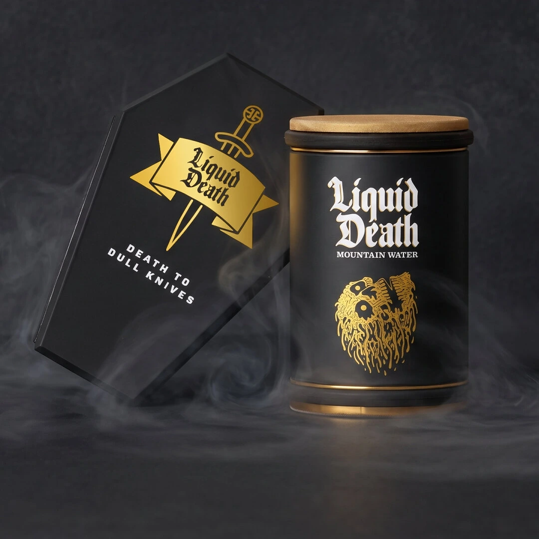 Black and gold Liquid Death rolling knife sharpener beside its coffin-shaped holder